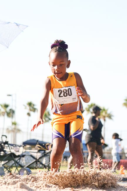 A little girl from CFY's Youth Athletics Program, jumping down with sand flying up in front of her feet.