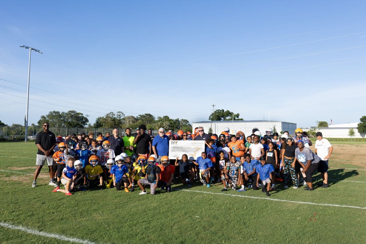 CFY Pinellas youth football team gathered together on a field during a game, holding a Grant check.