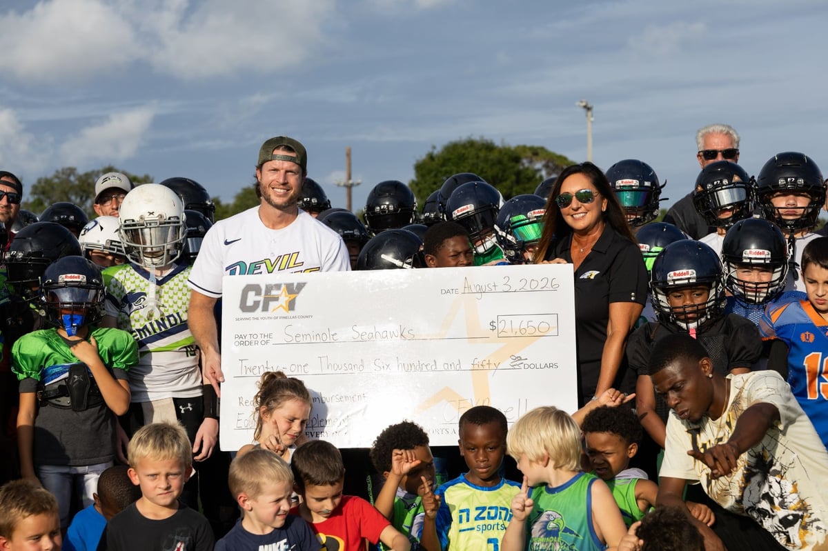 Youth football players from the Seminole Seahawks team on the field in Clearwater, Florida, holding a grant check.